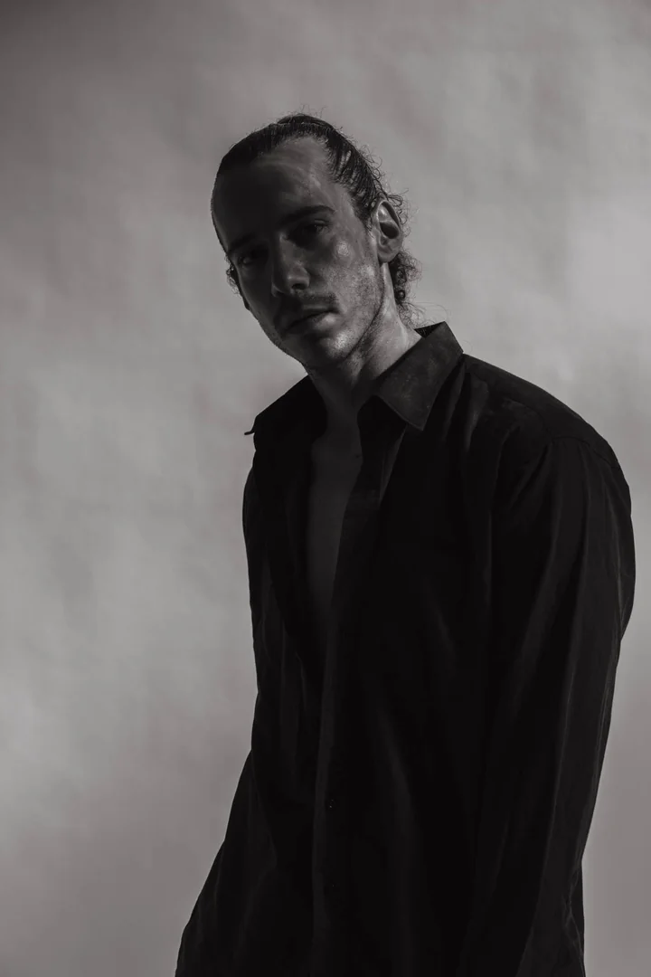 Zeyan Castracane. Standing at an angle in a black shirt. Black-and-white studio portrait.