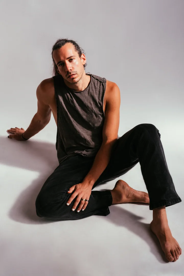 Full-length colour portrait of Zeyan seated barefoot against a pale studio backdrop.