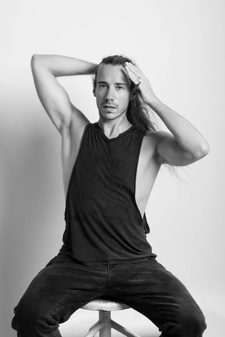 Zeyan Castracane. Seated with arms lifted to the hair. Black-and-white portrait.